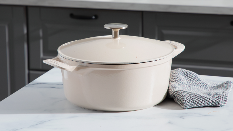 Product shot of the cream colored Made In Dutch Oven with lid on top of granite countertop next to gray dishcloths.