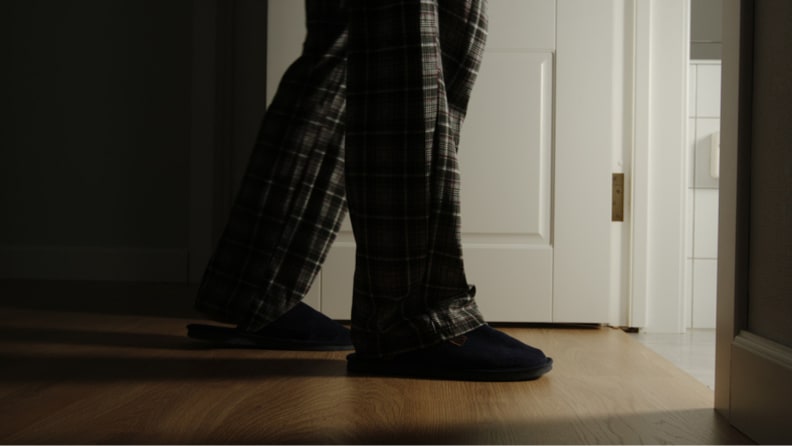 Man wearing pajama pants walking across hard wood floor.