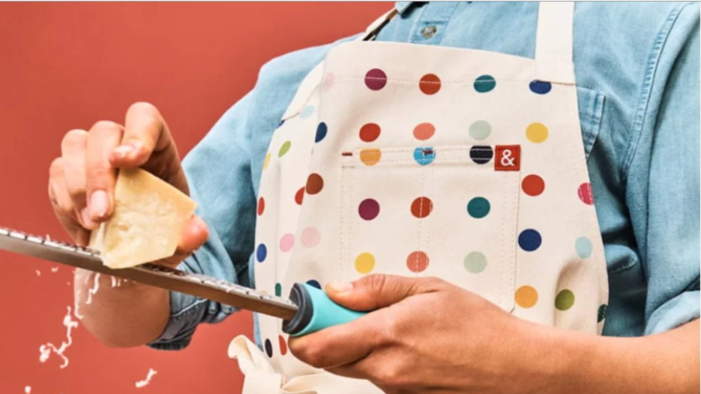 A close image of a person wearing a multicolored polka dot apron from Hedley and Bennett while cutting food.