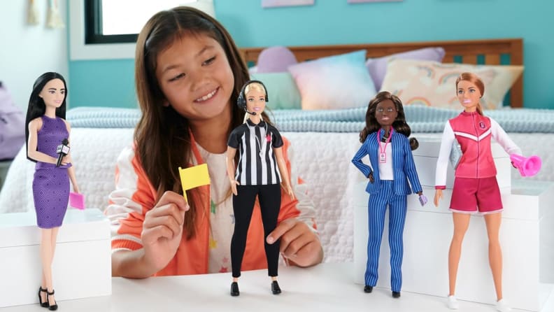 A smiling young girl plays with the four dolls of the Barbie Women in Sports set.