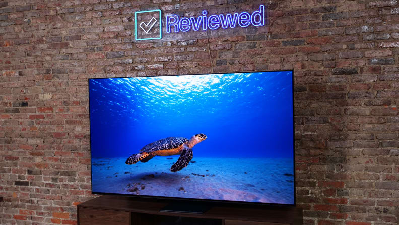 The Samsung S95C QD-OLED TV on an entertainment center next to a brick wall.