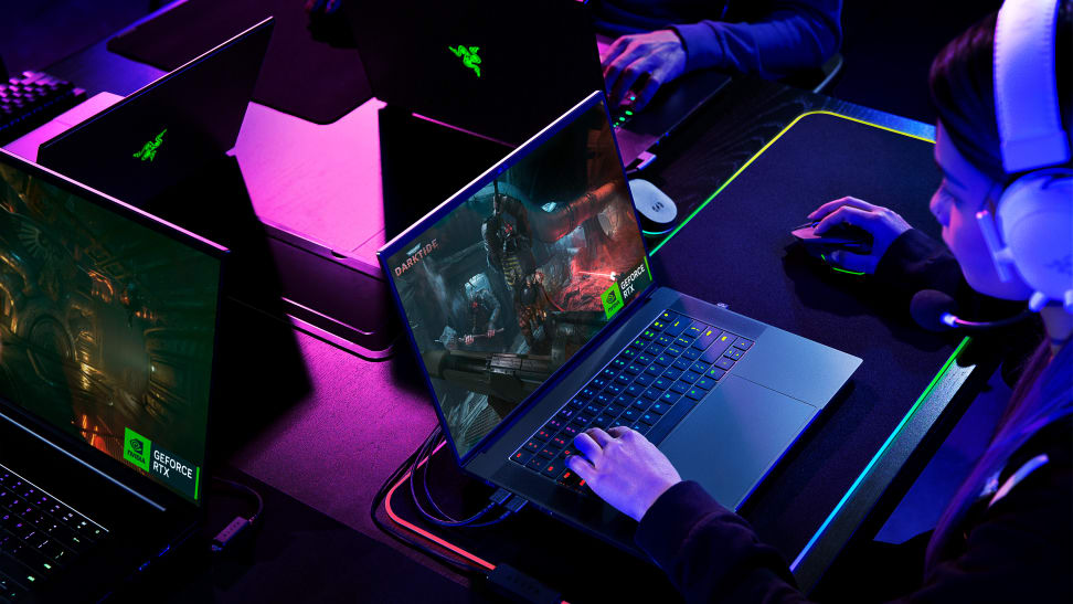 A person wearing a headset, sitting in front of a gaming laptop with soft neon light illuminating the background
