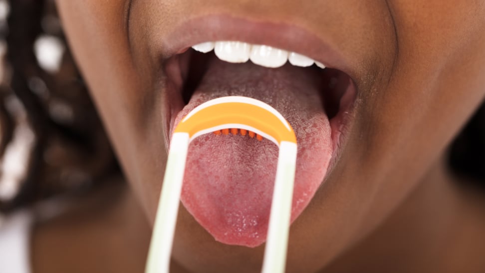 A woman scraping her tongue with an orange tongue scraper.