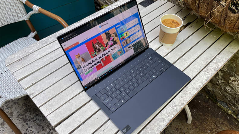 The Dell XPS 14 laptop opened to display a web browser on screen on a table outdoors next to a cup of iced coffee.