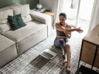 Person with prosthetic leg stretching on living room floor in front of laptop screen.