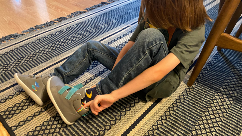 A child putting on grey high top sneakers.