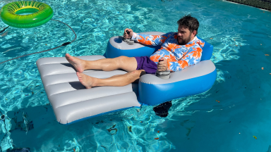 Person reclining on the inflated PoolCandy Splash Runner motorized pool float in middle of pool outdoors.