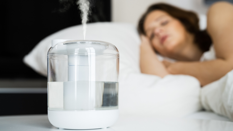 A person laying in bed with a humidifier on their nightstand.