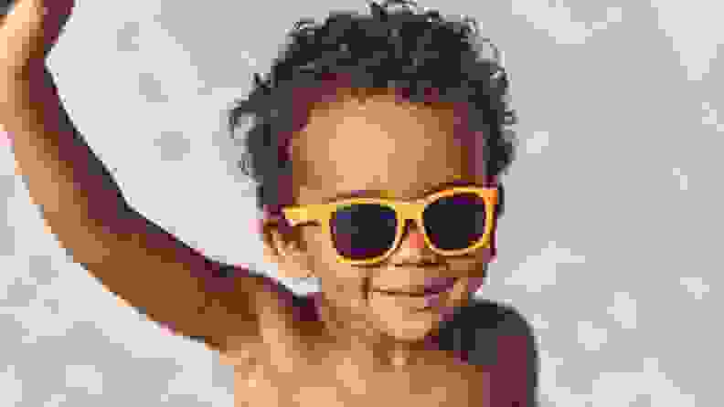 A young black child smiles at the beach with his cute sunglasses