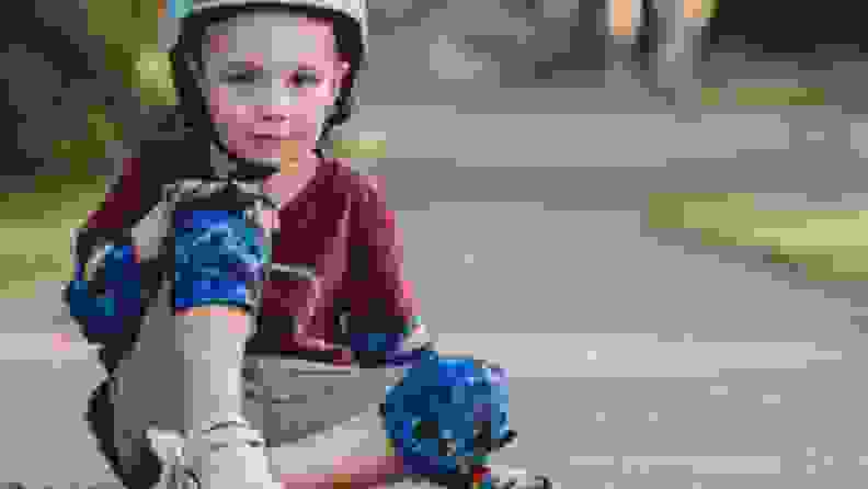 A boy sits on the ground wearing blue elbow and knee pads
