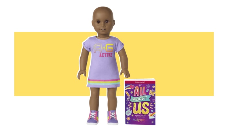 A bald American Girl doll with in a purple outfit, next to a book that says, "All About Us."
