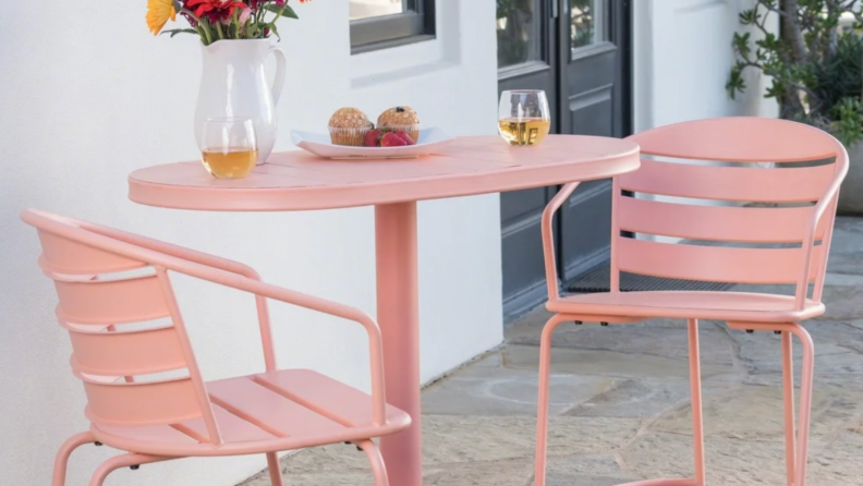 A pink bistro table and chairs sit on a patio.