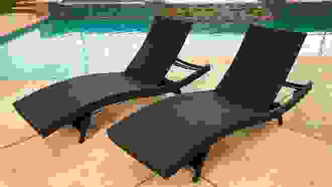 Two brown wicker patio chairs sitting on pool deck next to pool