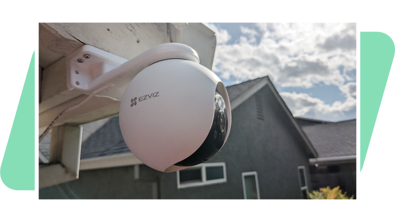The EzViz H8 Pro 3K outdoor camera mounted on a house with a green background.