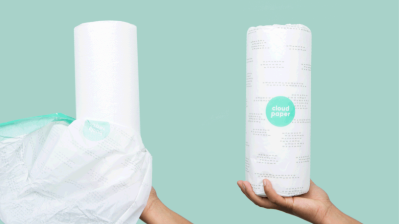 Product shot of Cloud Paper towels. On left, hand holding single unwrapped roll of bamboo cloud paper towels. On right, hand holding single wrapped roll of bamboo cloud paper towels.