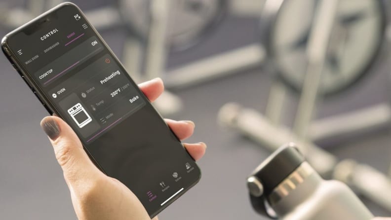 A person hold a smart phone in their hand and the screen displays the SmartHQ app in use.