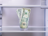 A close-up of the interior of an empty refrigerator with a glass of money on one shelf.