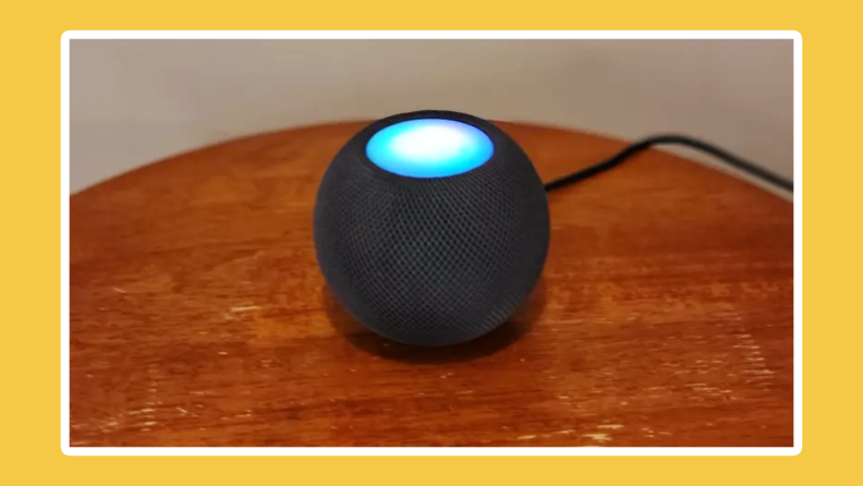 Apple HomePod Mini sitting on top of wooden surface with LED light lit up on top.