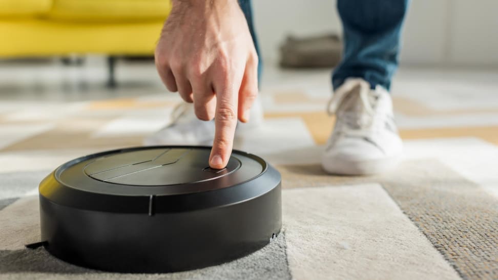 Cropped view of man pointing with finger at robotic vacuum cleaner in living room.