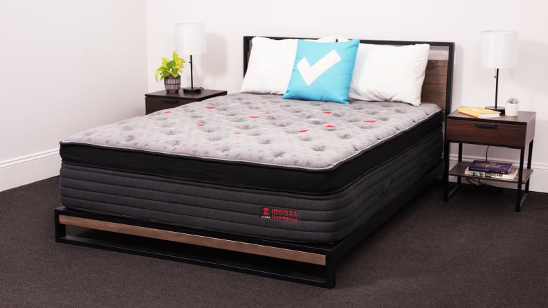The Zoma Boost mattress appears in a bedroom with bedside tables on either side.