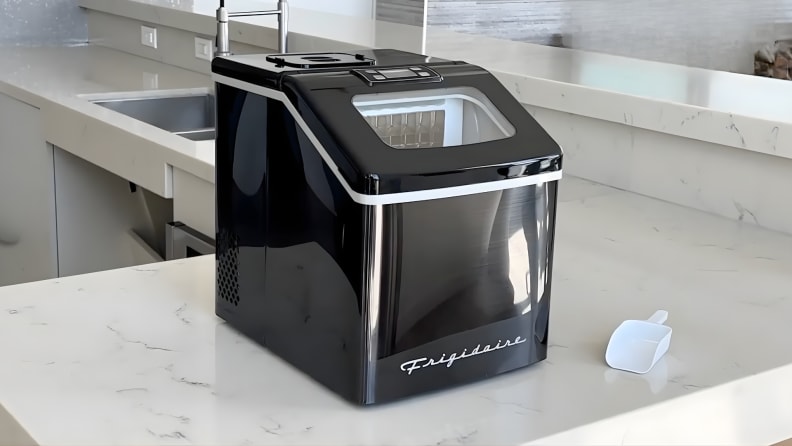 Frigidaire EFIC452 clear ice maker sitting on a kitchen countertop next to a plastic ice scoop.
