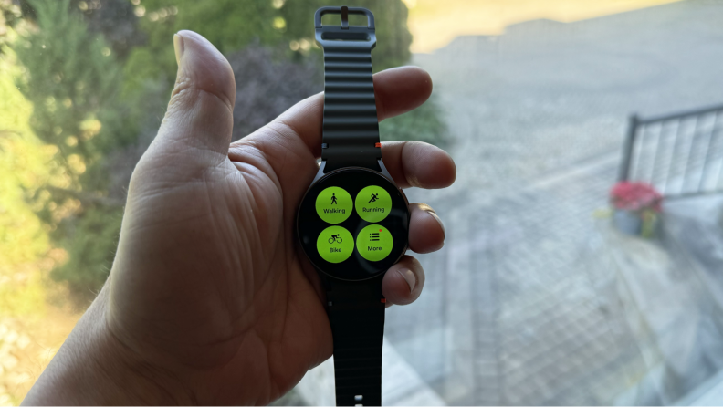 A hand holding up the smartwatch displaying a green menu.