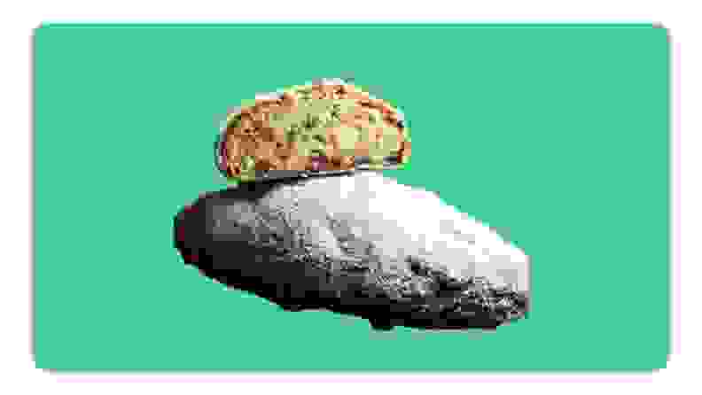 A whole powdered German stollen loaf next to one sliced in half in front of green background.