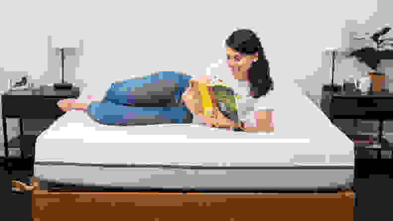 A woman reading a book, laying across a Purple mattress.