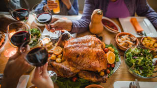 Hands raise red wine glasses over a Thanksgiving dinner table with a roasted turkey.