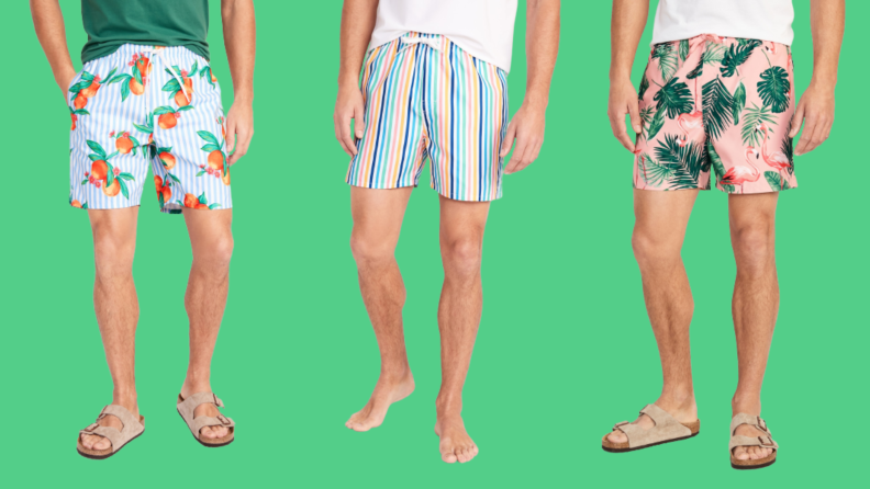 Three men's swimsuits: One with a fruit print against blue stripes, one in rainbow stripes, and one in a botanical print against a pink background.