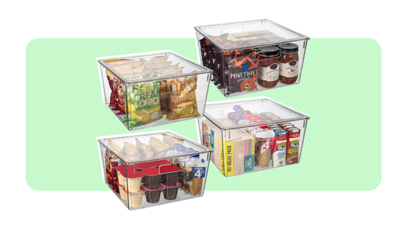 Four clear storage bins with lids filled with snacks in front of light green background.