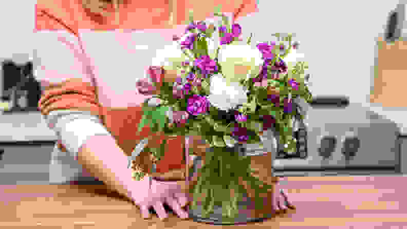 A person standing behind a vase of flowers on a countertop.