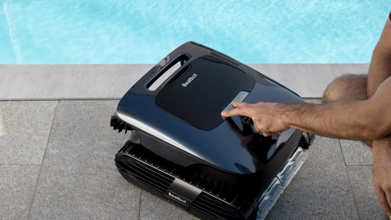 A black, square robot sits by a pool while an arm presses buttons on it