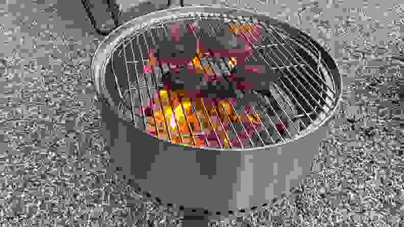 Burger patties cook on a grate over a charcoal grill.