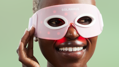 Woman wearing Solawave red light therapy eye mask on green background.