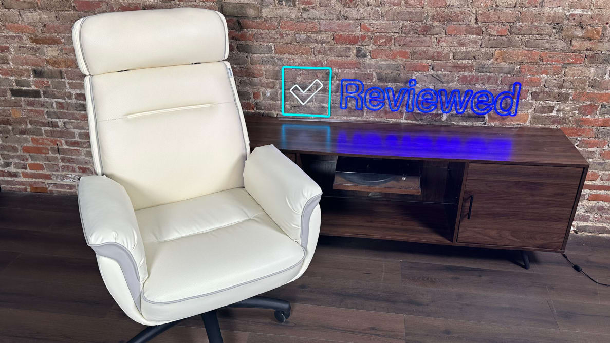 A close-up of the Eureka Royal Executive Home Office Chair against a brick wall. Behind it is a table holding up the Reviewed logo.