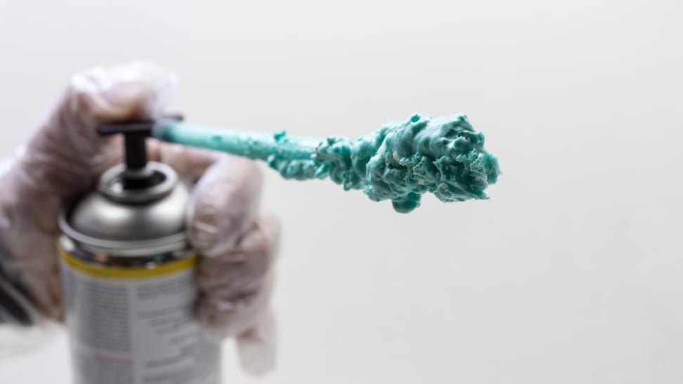 A gloved hand spraying spray foam insulation in a teal color