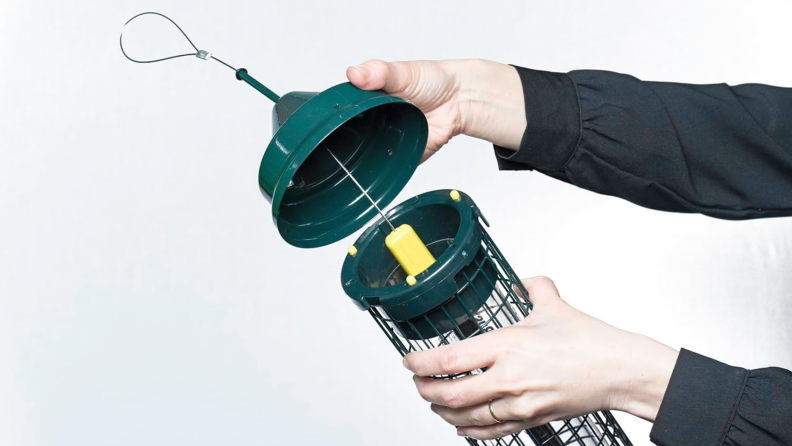 Two hands hold the Squirrel Buster Classic, opening it to show the squirrel-busting mechanism inside.