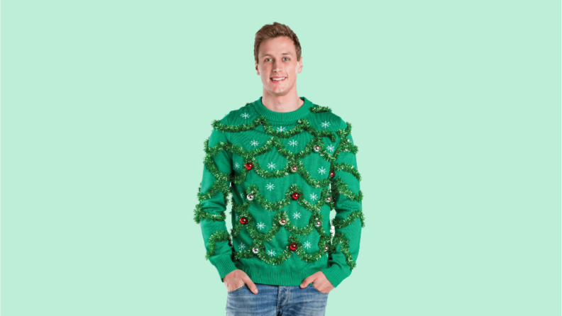 A man wears a green sweater festooned with green tinsel.