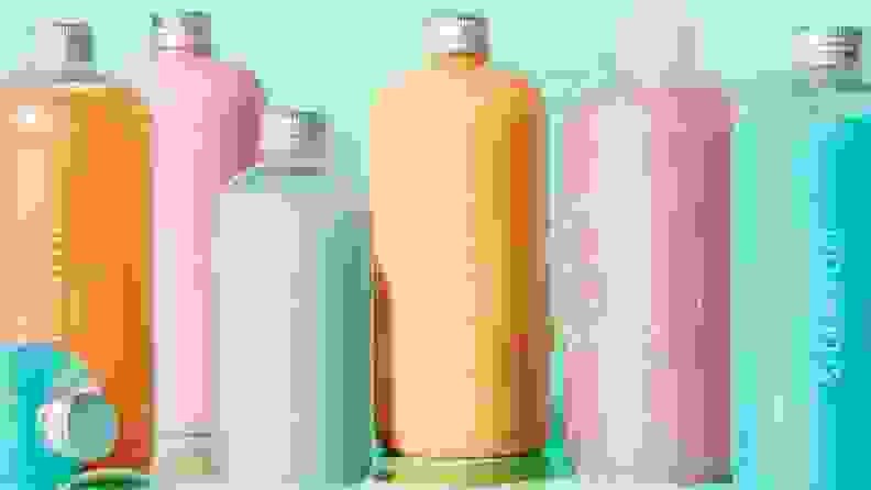 Multi-colored hair product bottles together in front of a green backround.