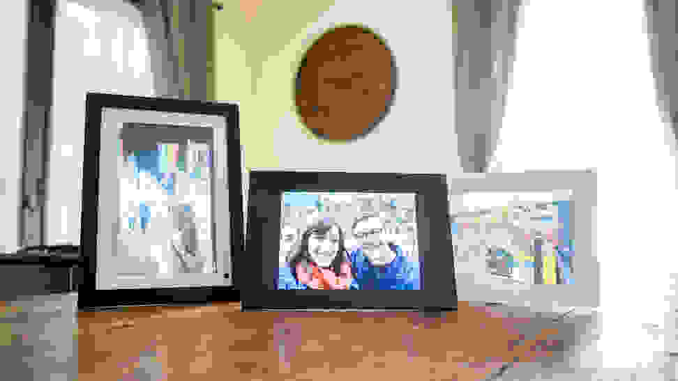 Three digital picture frames displaying family photos sit on a wooden table.