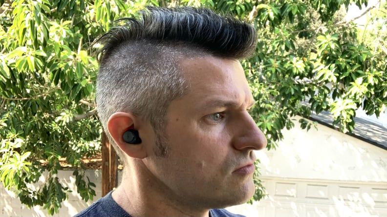 A man wearing the Anker Soundcore Space A40 earbuds while standing outside in front of a tree.`