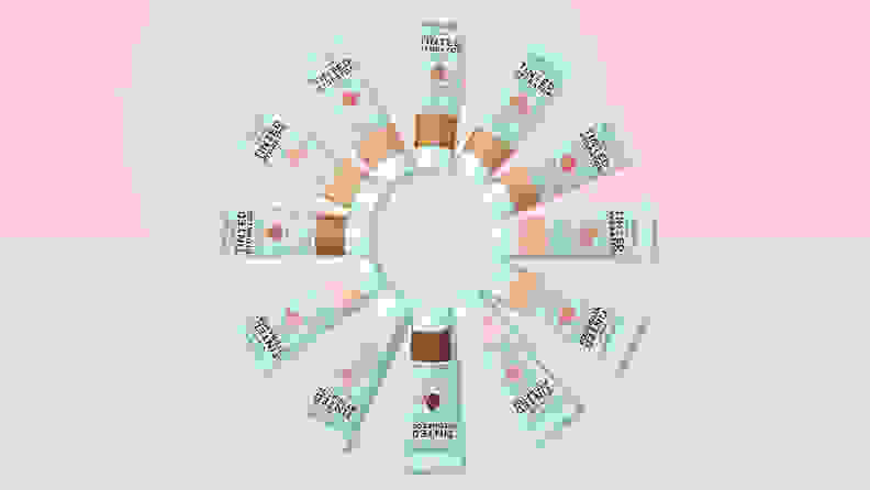 A circle of 12 Wet n Wild Bare Focus Tinted Hydrators on a blue and pink background.