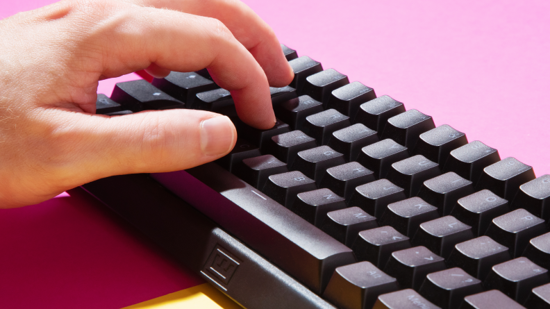 A closeup of a hand typing on a black wooting 60he keyboard
