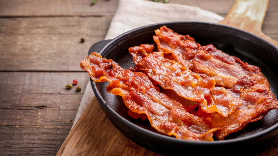 Strips of bacon in a skillet on a wooden board