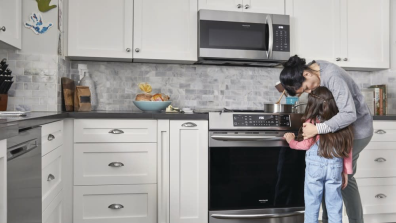 A parent helps a child in a kitchen.