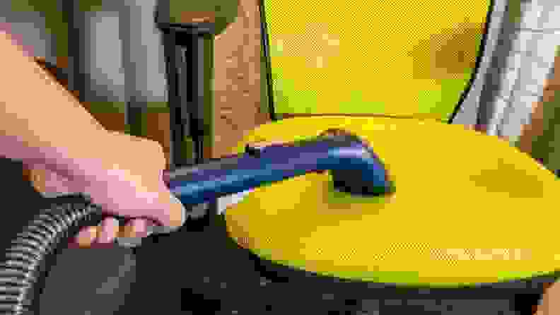 Person using hose attachment from the Eureka NEY100 carpet cleaner on the seat of a bright yellow office chair.