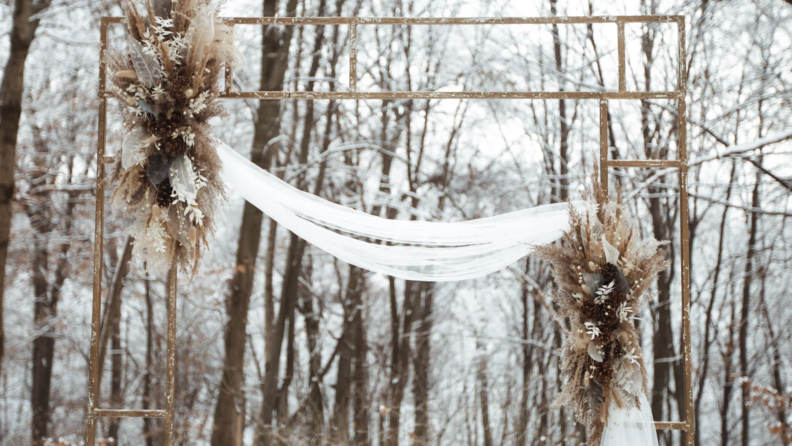 Tan flower arch arrangement in snowy outdoor setting.