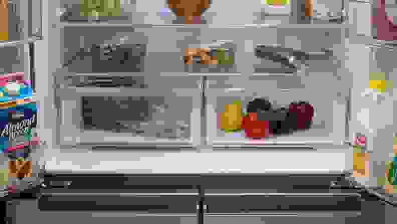 A close-up of the Whirlpool WRQA59CNKZ's crisper drawers. The fridge is fully stocked with food, and the crispers hold various fruits and vegetables.