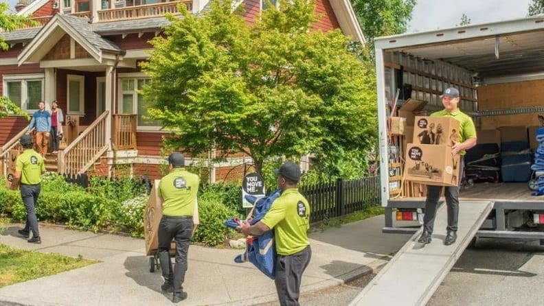 Four movers unloading and bringing boxes to the couple's new home